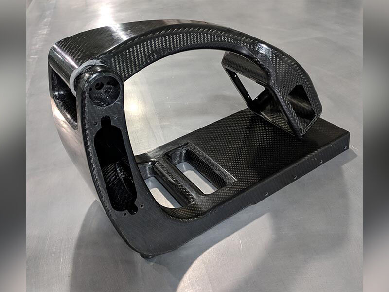 Image of the carbon fiber body of the portable X-ray machine attached at a hinge and folded. The device is sitting on a steel table surface. The surface of the device shows a carbon fiber weave with a high-gloss finish.